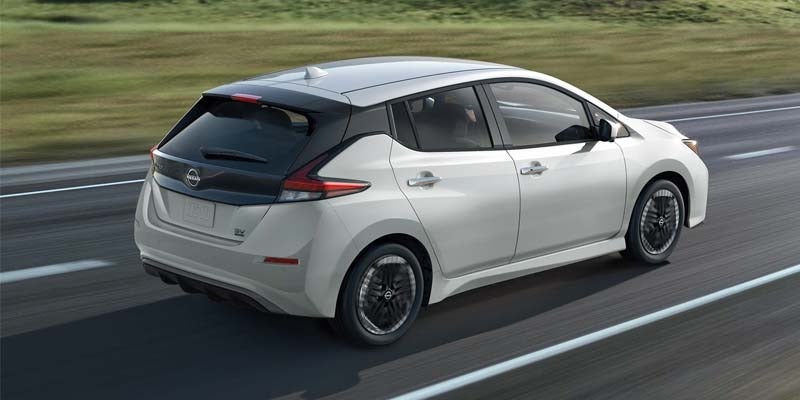 rear right angle view of a white 2024 nissan leaf driving down a street