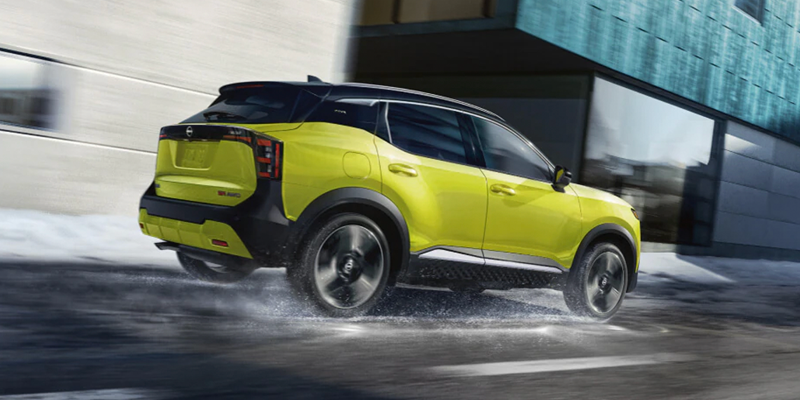 Lime yellow Nissan Kicks driving through wet, slushy winter streets next to modern buildings.