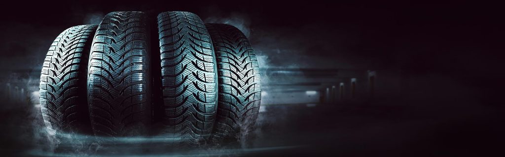 Four car tires lined up on a dark, smoky background