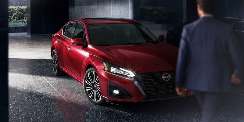 a red 2024 nissan altima parked in a sleek and modern garage and in the foreground a man in a blue suit walking towards it