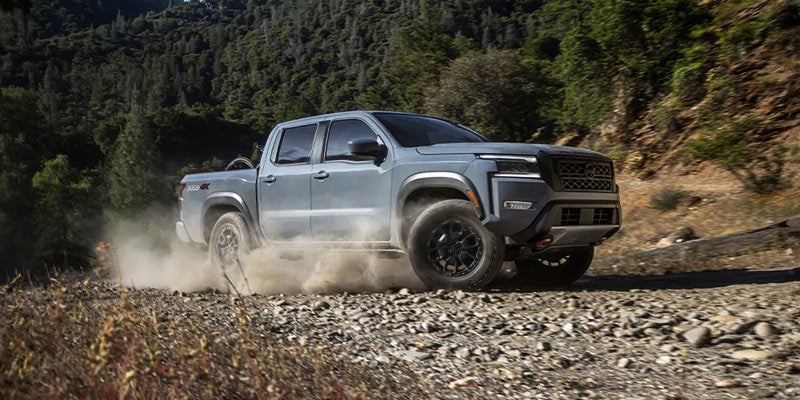 gray 2024 nissan frontier driving through a dirt country road