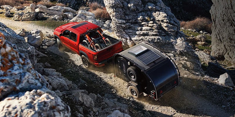 birds eye view of a red 2024 nissan frontier hauling a small trailer through rocky terrain