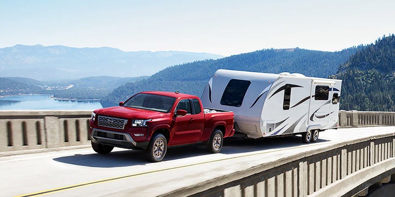 red 2024 nissan frontier driving through a bridge towing an rv