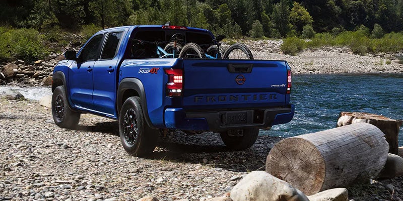 blue 2024 nissan frontier parked on a lake shore with some mountain bikes in the truck bed