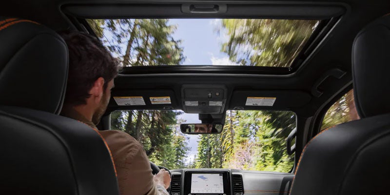 a backseat perspective of the interior front cabin of the 2024 nissan frontier, showing a man in the drivers seat