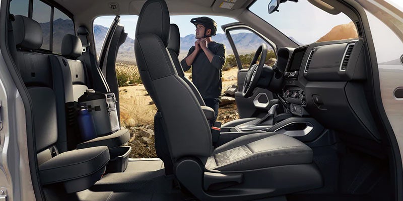 side profile view of the left hand side of the 2024 nissan frontier with a man standing by the drivers seat putting on a bike helmet