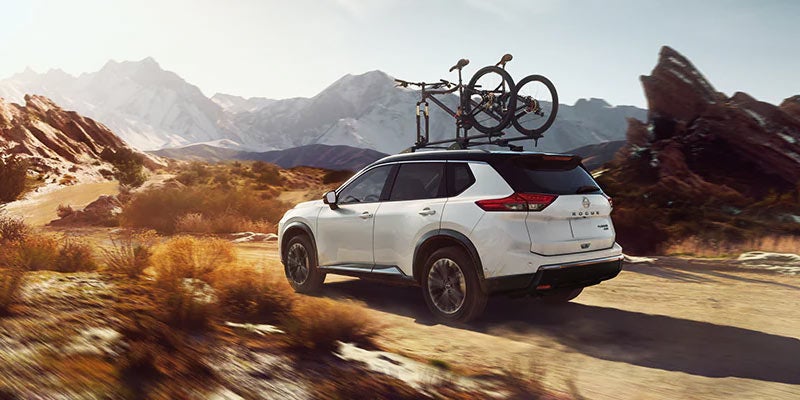 white 2024 nissan rogue with to bikes on the roof rails driving on a dirt road