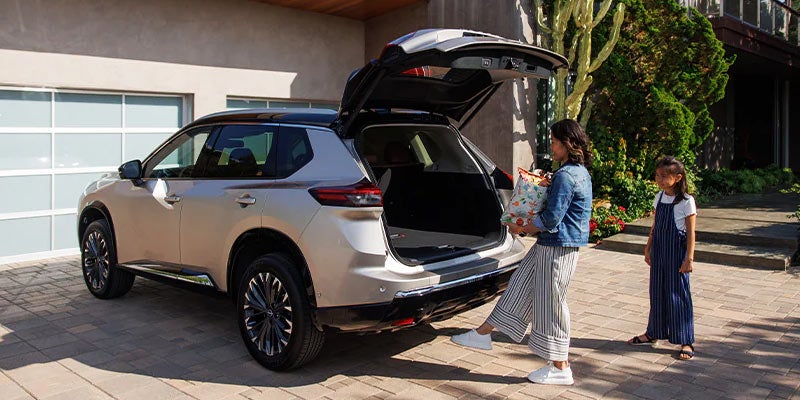 a woman carrying boxes using the motion sensor on the hatchback trunk of a 2024 nissan rogue to open it hands free