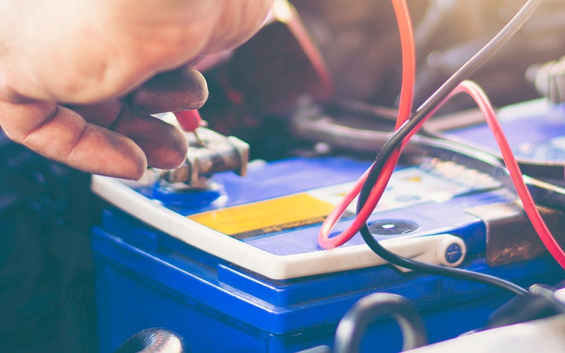 Car battery inspection with jumper cables connected during vehicle maintenance